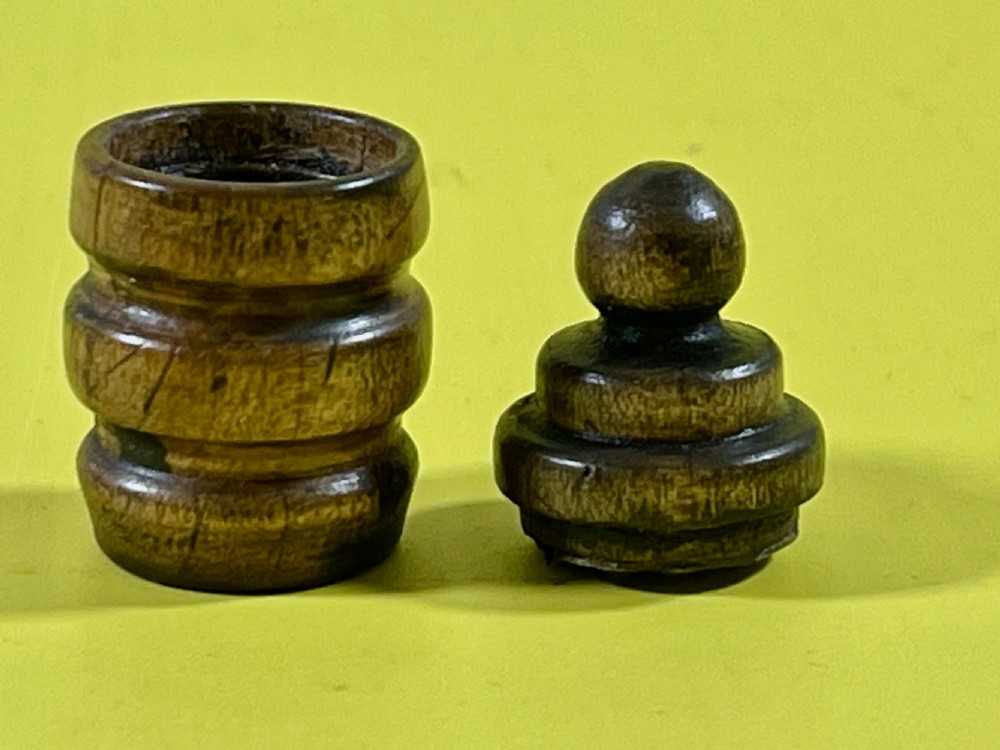 A small, cylindrical turned wooden snuff box with a matching lid, displayed on a yellow surface.