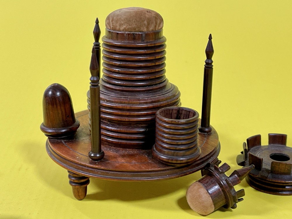 An antique turned rosewood sewing companion featuring a central turret-shaped spool holder surrounded by turned finials and sewing tools on a circular base with feet. View IV