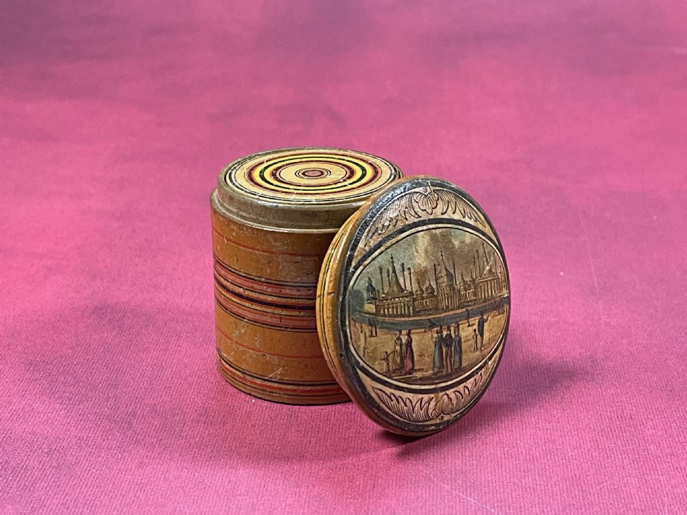 A graduated set of seven cylindrical turned whitewood stacking pots featuring a printed landscape view on the largest lid and concentric coloured circles on the smaller lids. View III