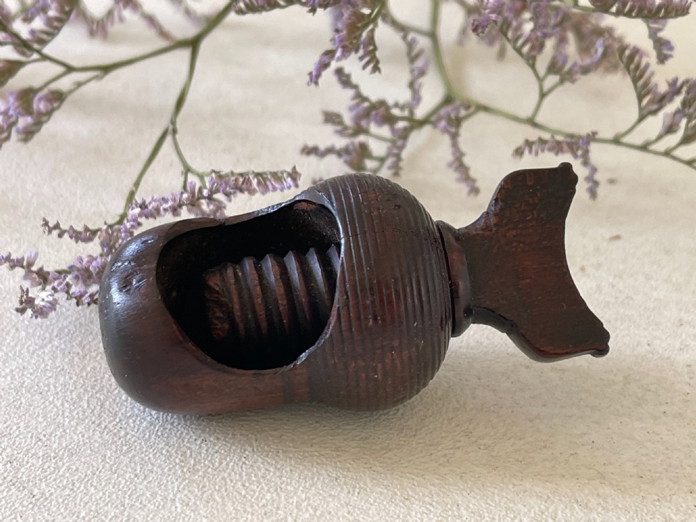 A dark carved wooden acorn-shaped nutcracker featuring an internal screw mechanism and a turned handle lying horizontally.