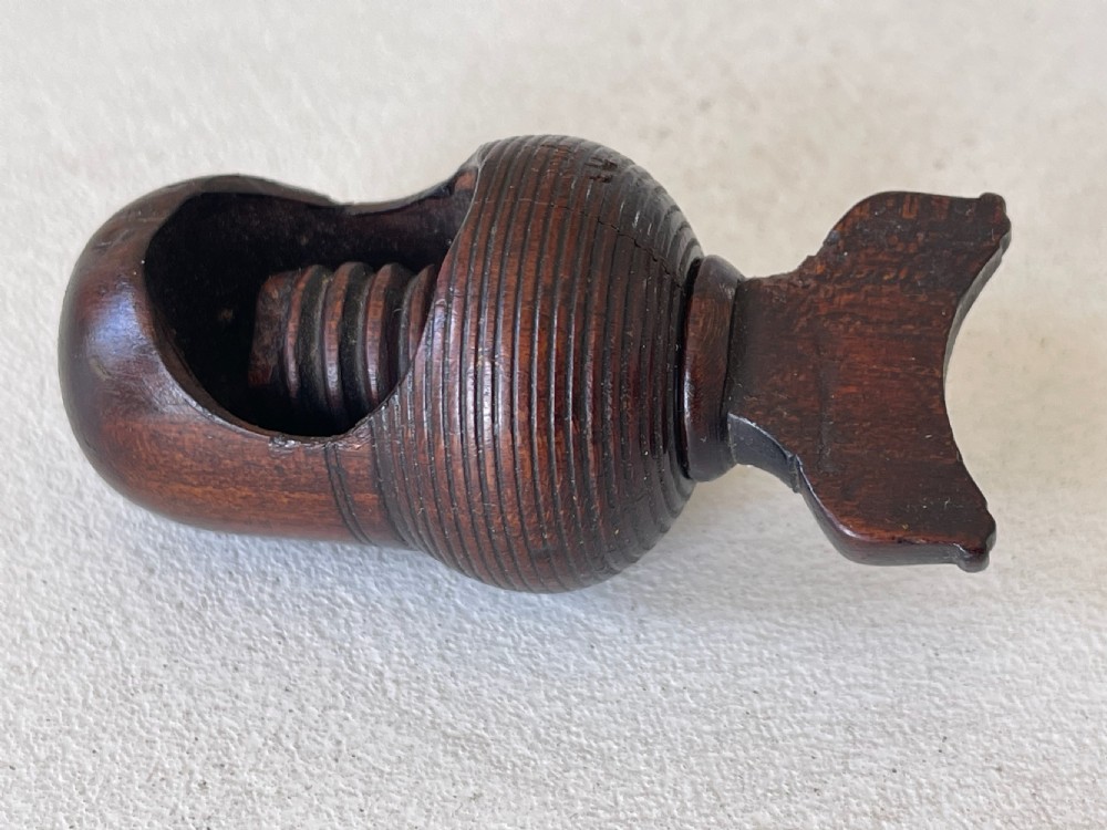A dark carved wooden acorn-shaped nutcracker featuring an internal screw mechanism and a turned handle lying horizontally. View II