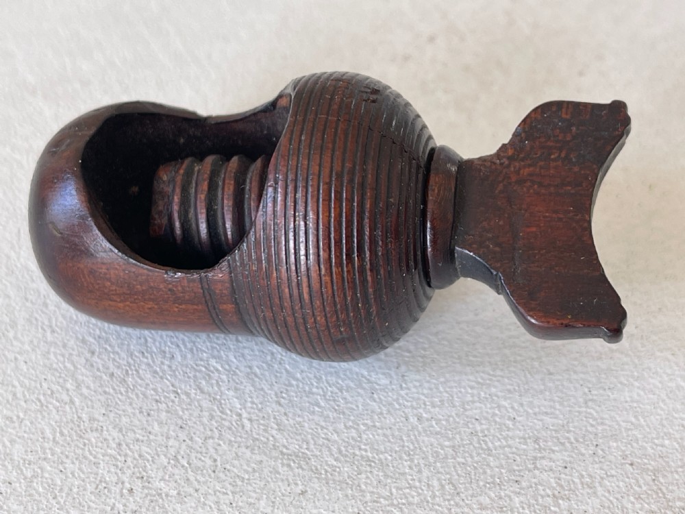 A dark carved wooden acorn-shaped nutcracker featuring an internal screw mechanism and a turned handle lying horizontally. View III