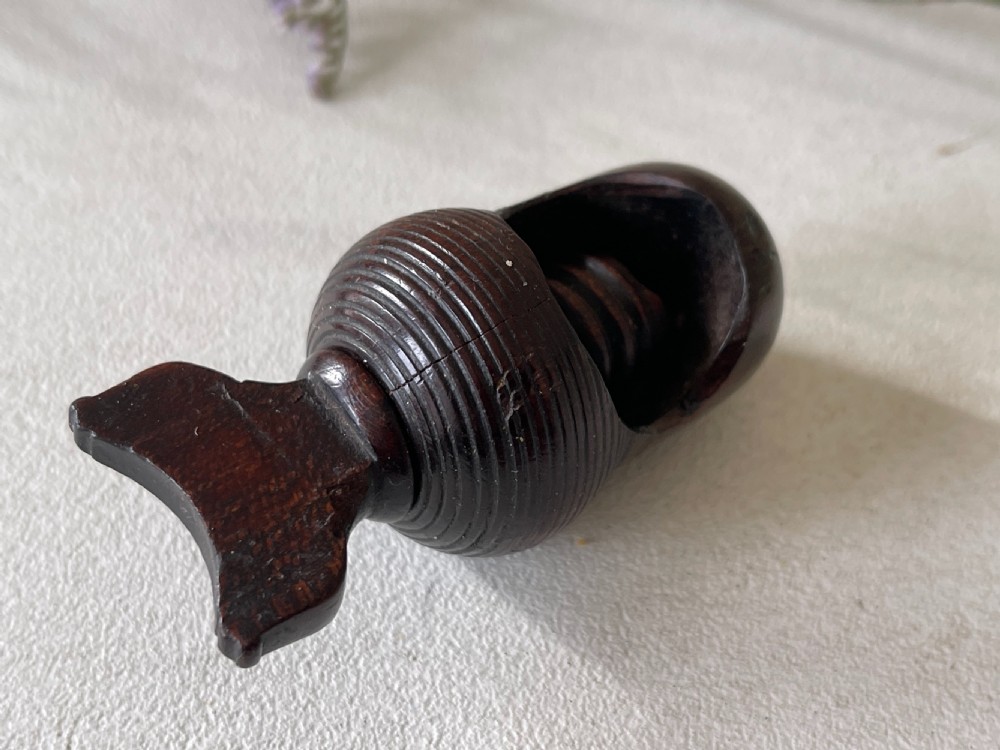 A dark carved wooden acorn-shaped nutcracker featuring an internal screw mechanism and a turned handle lying horizontally. View V
