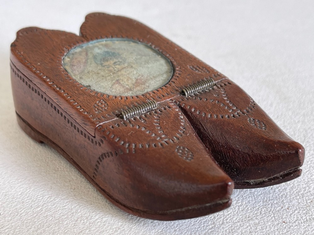 An antique double shoe-shaped wooden snuff box featuring carved pinwork pattern, wire spring hinges, and an inset glazed portrait miniature.
