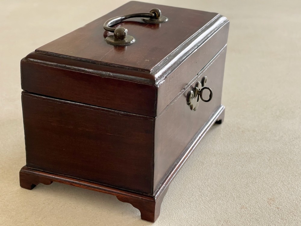 A small dark brown mahogany tea caddy with a brass keyhole escutcheon and a top handle, resting on bracket feet. View II