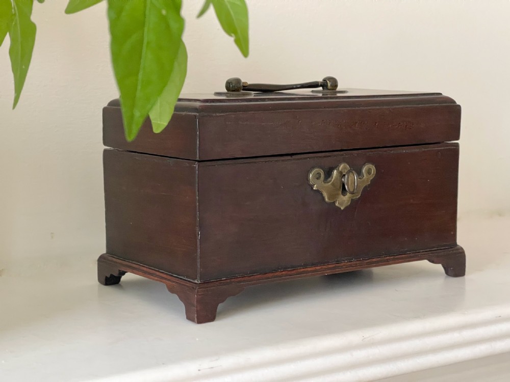 A small dark brown mahogany tea caddy with a brass keyhole escutcheon and a top handle, resting on bracket feet. View IV