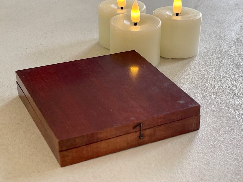 An open square mahogany wooden box containing a circular magnetic compass with a printed compass rose card and brass hook latch. View III