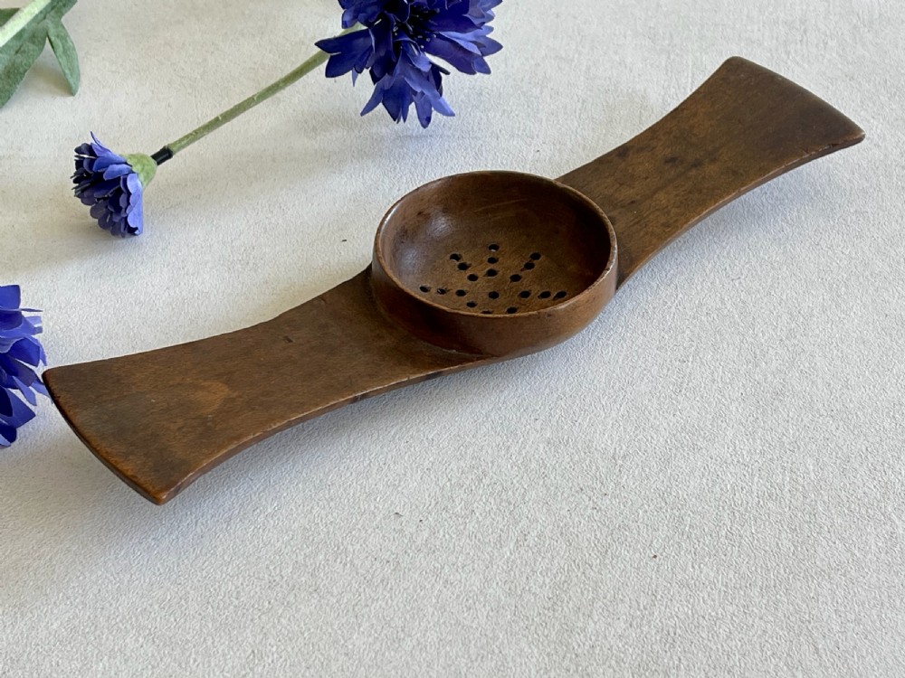 An antique carved wooden Negus strainer with a central perforated circular bowl and flared flat side handles.