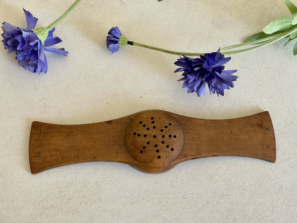 An antique carved wooden Negus strainer with a central perforated circular bowl and flared flat side handles. View II