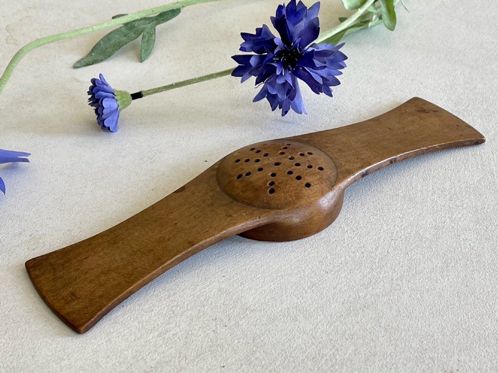 An antique carved wooden Negus strainer with a central perforated circular bowl and flared flat side handles. View IV