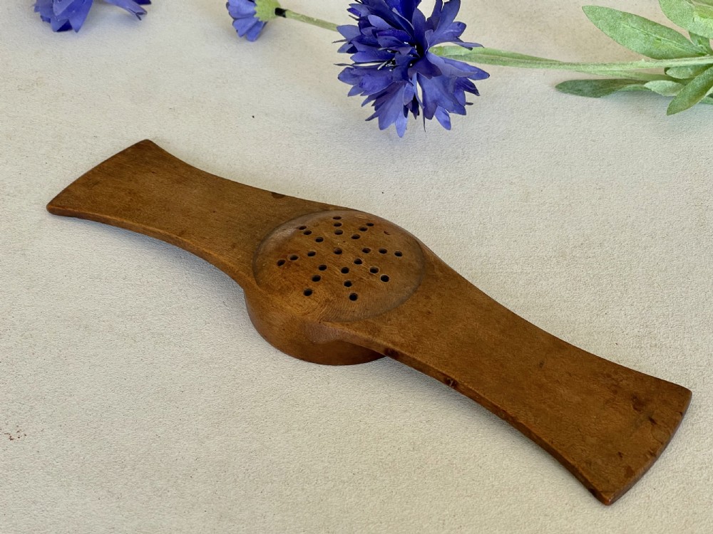 An antique carved wooden Negus strainer with a central perforated circular bowl and flared flat side handles. View V