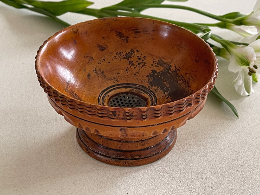 A small turned warm brown wooden Georgian searce with a carved wavy rim, pedestal base, and perforated strainer bottom.