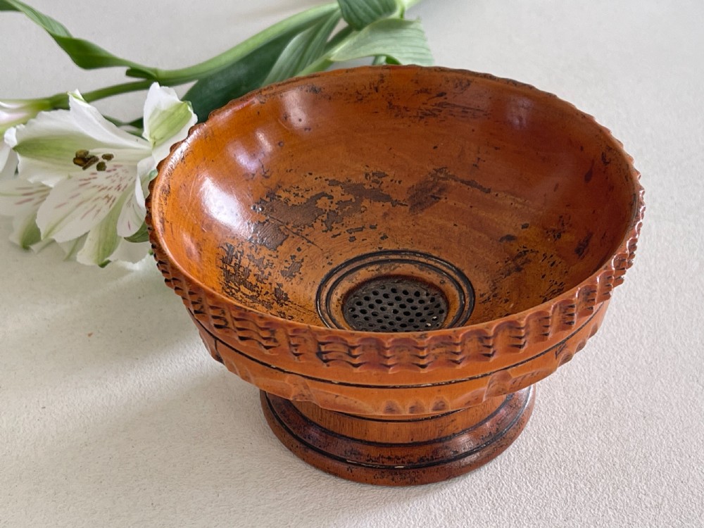 A small turned warm brown wooden Georgian searce with a carved wavy rim, pedestal base, and perforated strainer bottom. View III