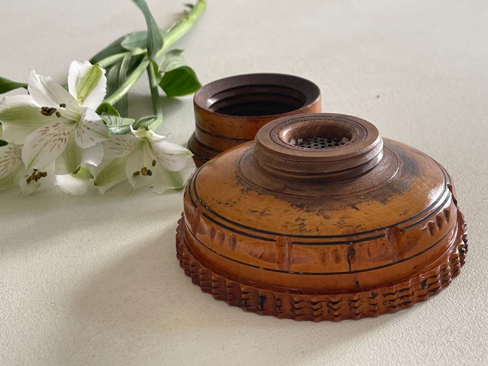 A small turned warm brown wooden Georgian searce with a carved wavy rim, pedestal base, and perforated strainer bottom. View X