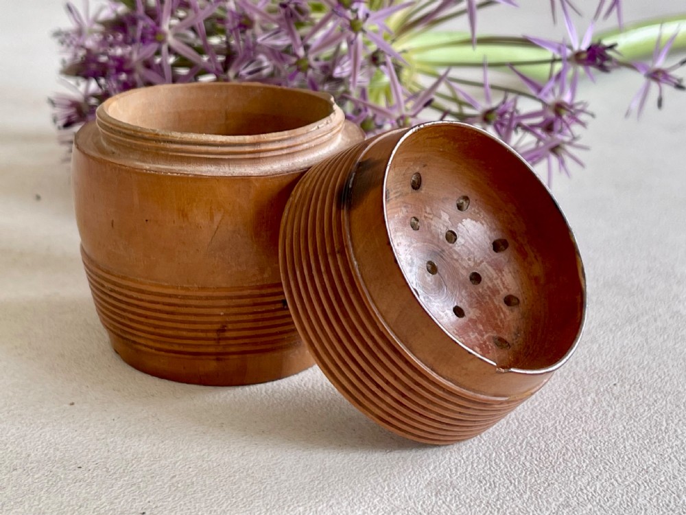 A small turned wooden pounce pot displaying a reeded base and a perforated concave top lid.