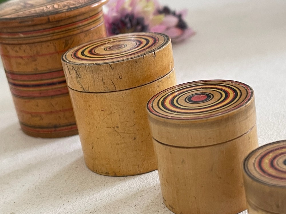 A set of seven turned natural wood nesting pots featuring colourful concentric painted rings on the lids and a printed landscape on the largest cover. View III