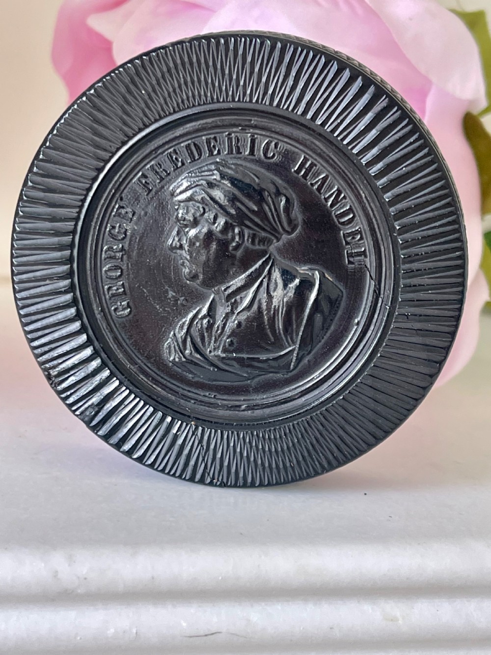 A circular black pressed composition antique snuff box lid depicting a bas-relief profile portrait of George Frederic Handel.
