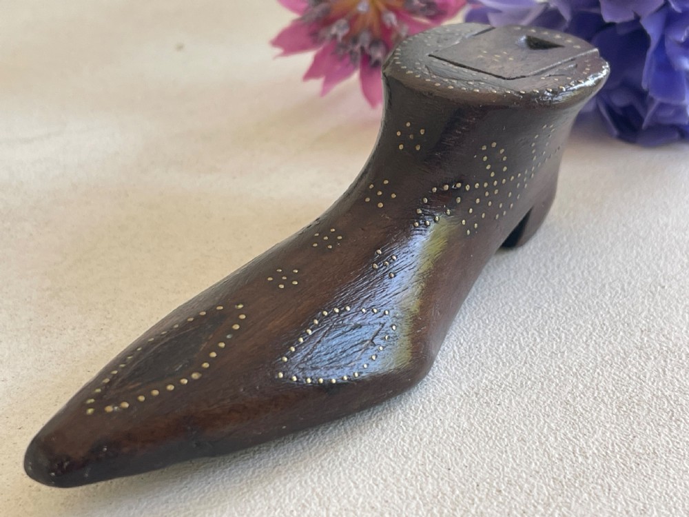 A carved dark wood snuff box fashioned in the shape of a shoe, decorated with brass pinwork floral patterns and a sliding lid on top.