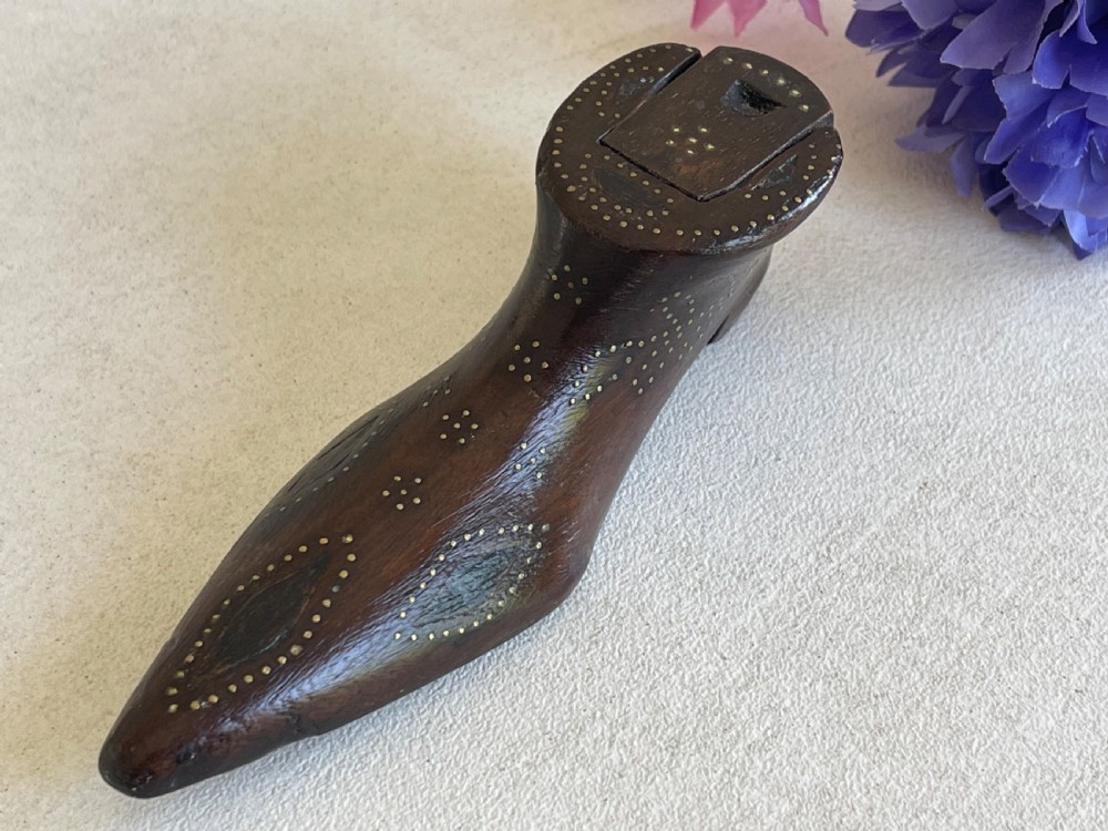 A carved dark wood snuff box fashioned in the shape of a shoe, decorated with brass pinwork floral patterns and a sliding lid on top. View V