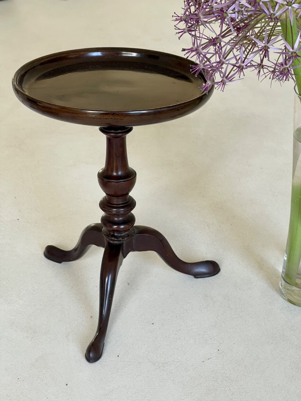 A small dark brown antique wooden tripod candle stand featuring a round dished top and cabriole legs.