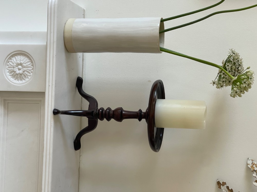 A small dark brown antique wooden tripod candle stand featuring a round dished top and cabriole legs. View II