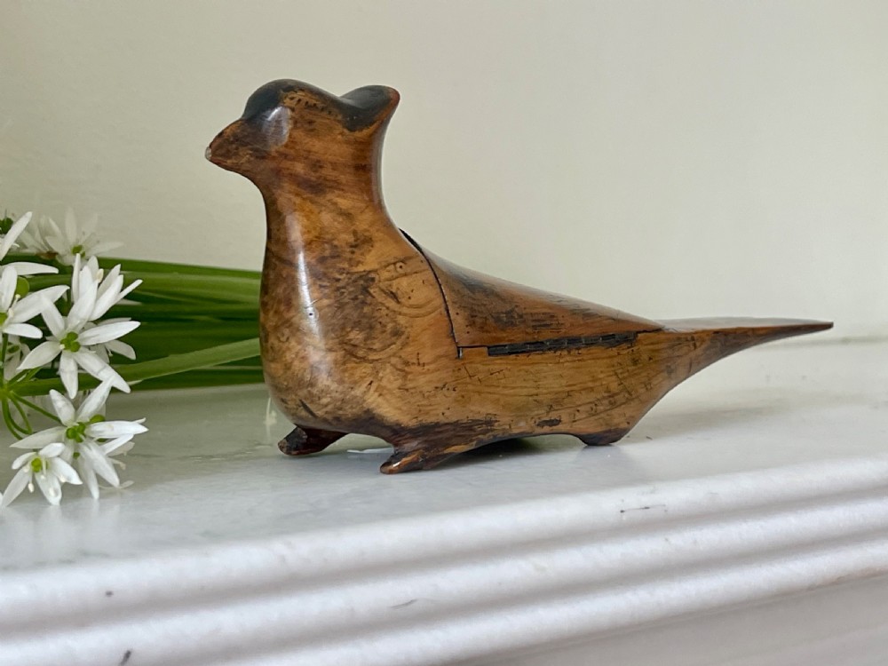 A small hand-carved wooden snuff box shaped like a bird with a polished natural timber grain and integrated hinged lid.