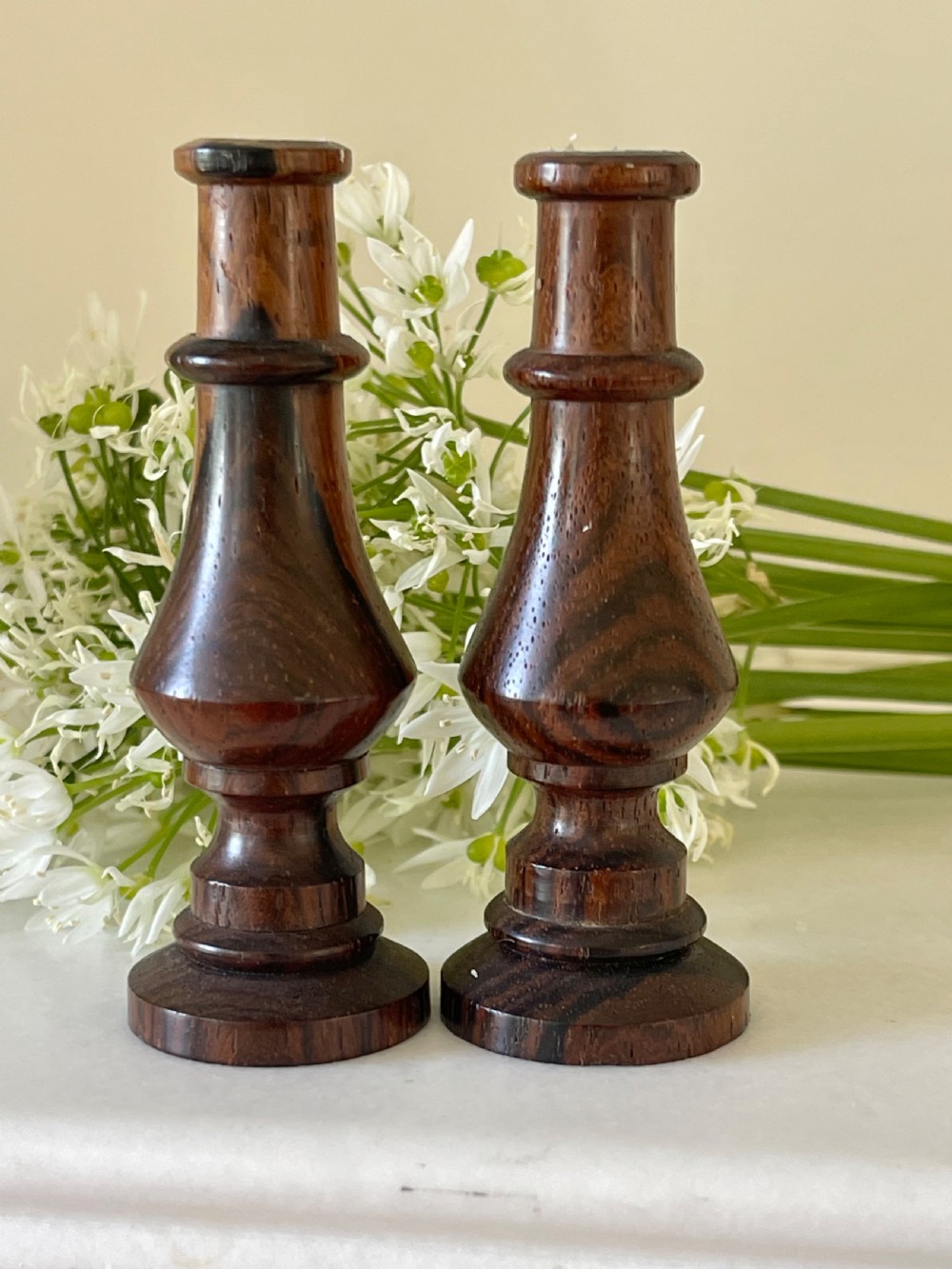 A pair of small turned dark wood taper candlesticks featuring baluster-shaped shafts and circular flat bases.