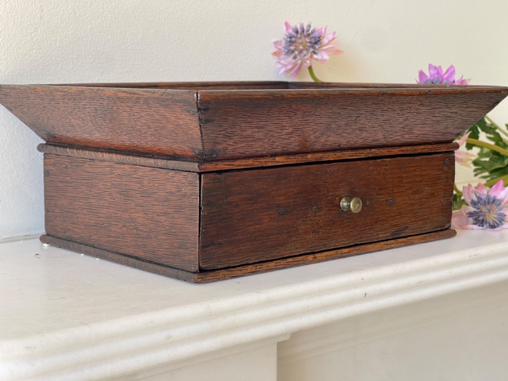 A dark oak rectangular desk tidy featuring a wide flared top tray above a single drawer fitted with a small brass knob.