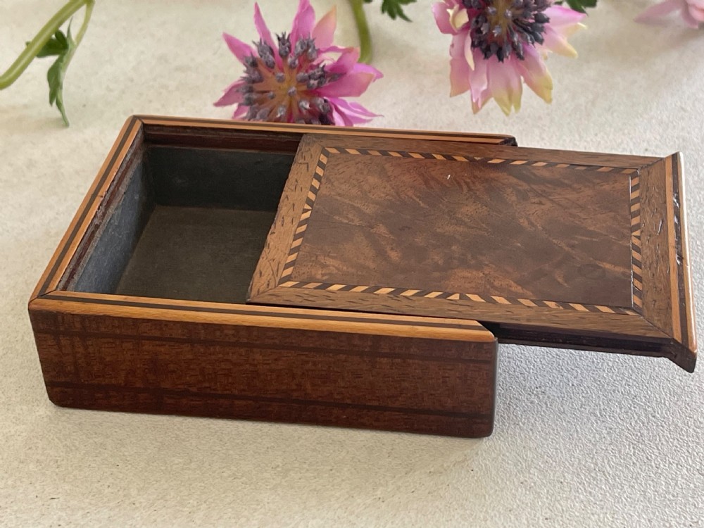A small rectangular brown timber snuff box featuring a sliding lid with geometric chevron inlay detailing.