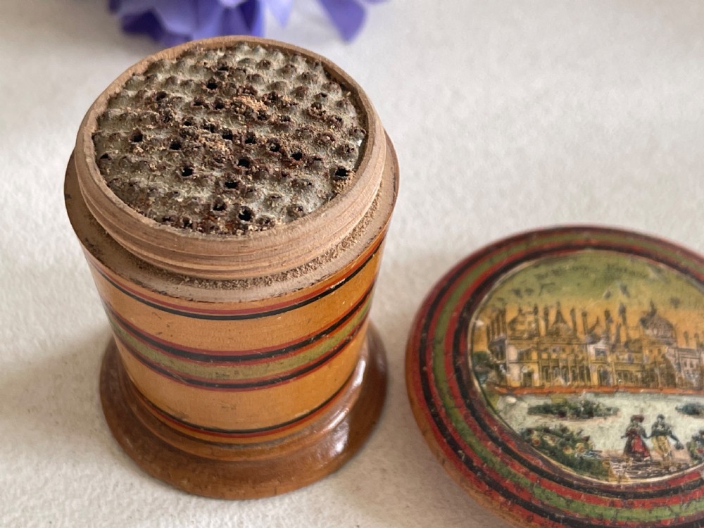 A small turned wooden Georgian nutmeg grater featuring painted red and green stripes around its cylindrical body and a circular printed landscape scene on the lid. View III