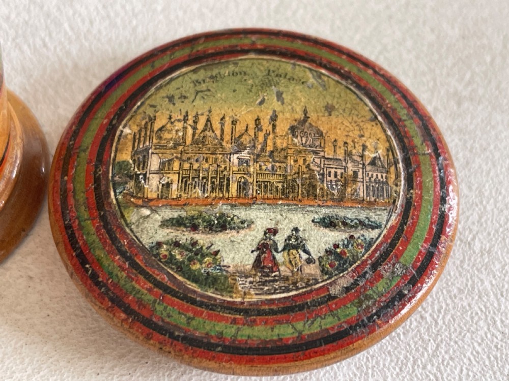 A small turned wooden Georgian nutmeg grater featuring painted red and green stripes around its cylindrical body and a circular printed landscape scene on the lid. View VI