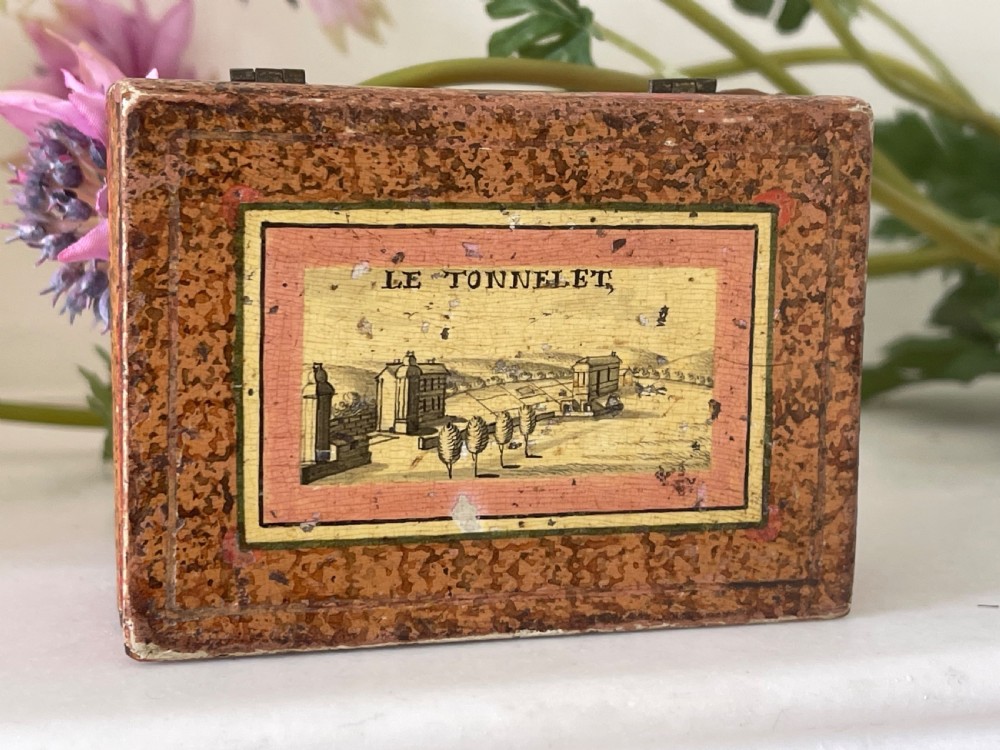 A small rectangular antique box constructed in the shape of two stacked books with red and gold patterned covers and exterior brass hinges. View VII