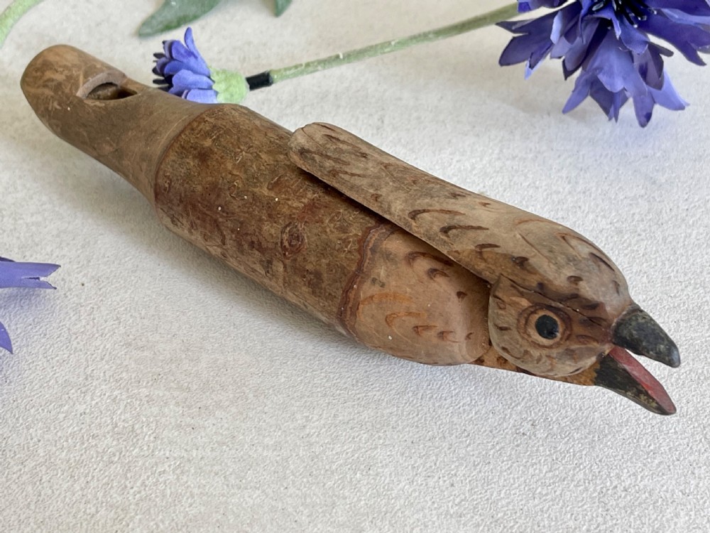 An antique carved wooden bird whistle with painted details resting on a textured surface.