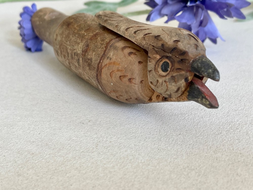An antique carved wooden bird whistle with painted details resting on a textured surface. View VI