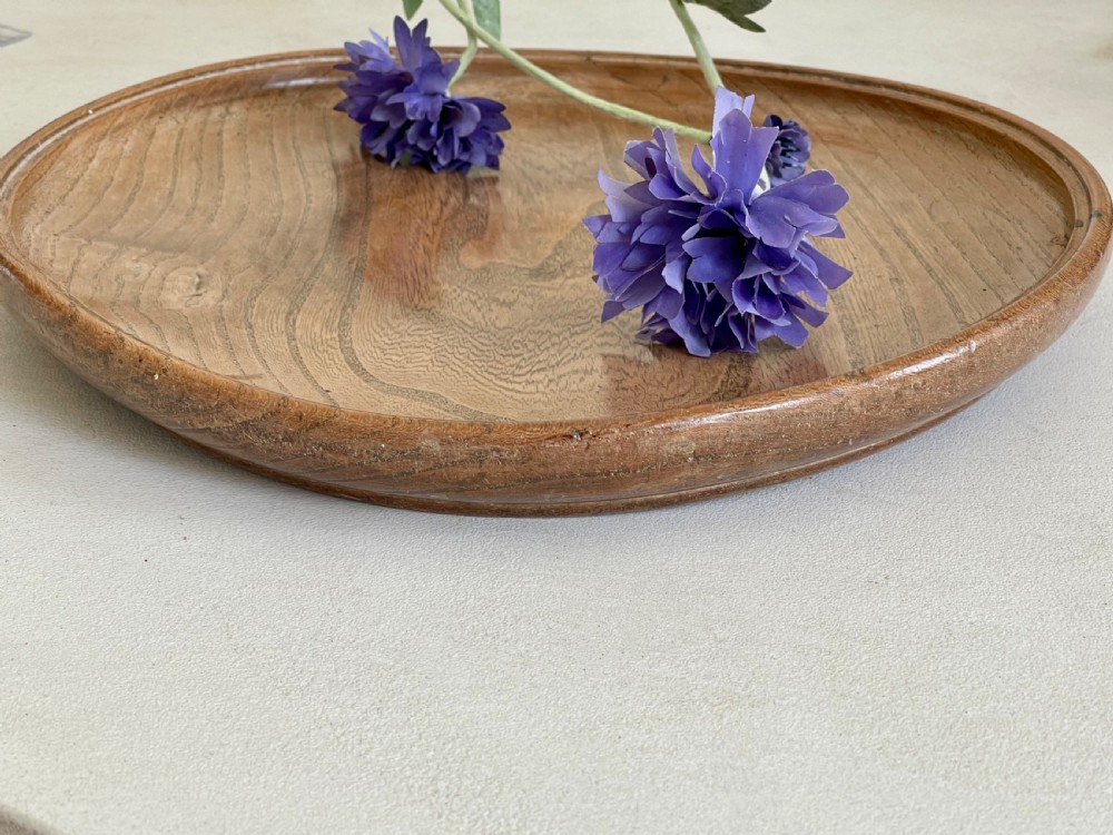 A large, shallow circular antique platter crafted from turned ash wood displaying prominent natural grain patterns.