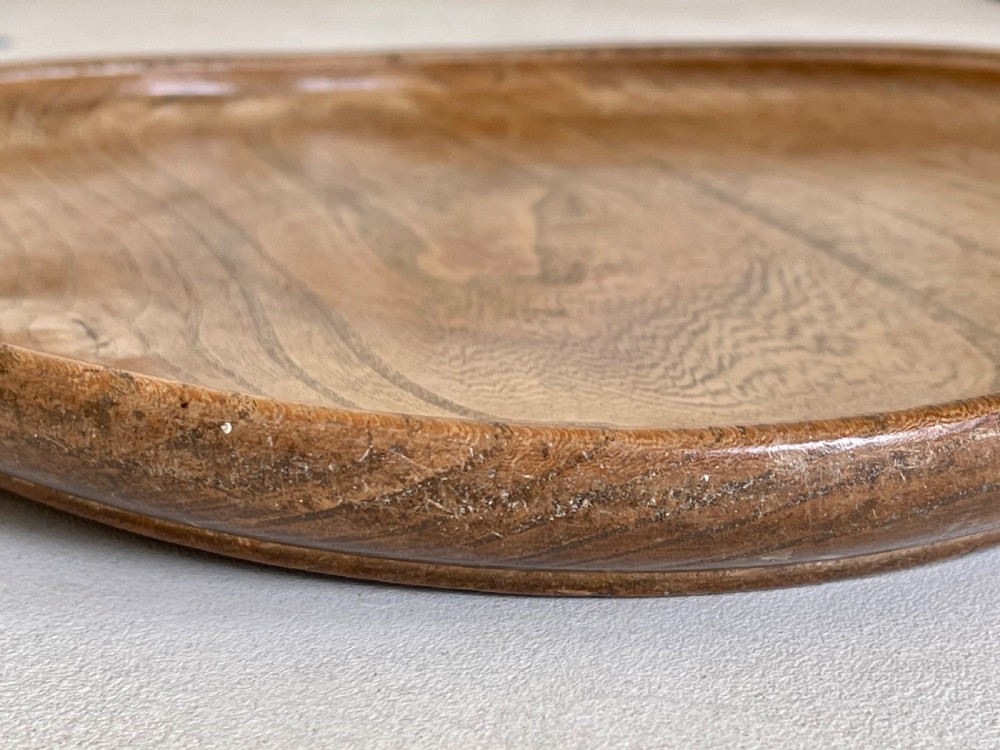A large, shallow circular antique platter crafted from turned ash wood displaying prominent natural grain patterns. View III