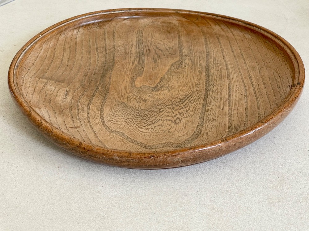 A large, shallow circular antique platter crafted from turned ash wood displaying prominent natural grain patterns. View IV