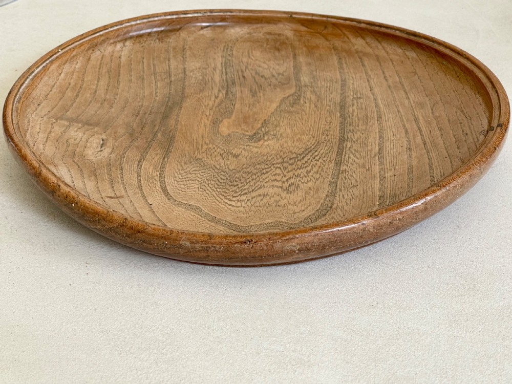 A large, shallow circular antique platter crafted from turned ash wood displaying prominent natural grain patterns. View V