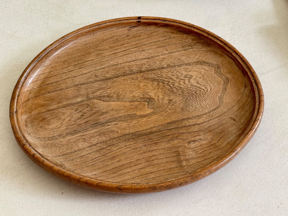 A large, shallow circular antique platter crafted from turned ash wood displaying prominent natural grain patterns. View VI