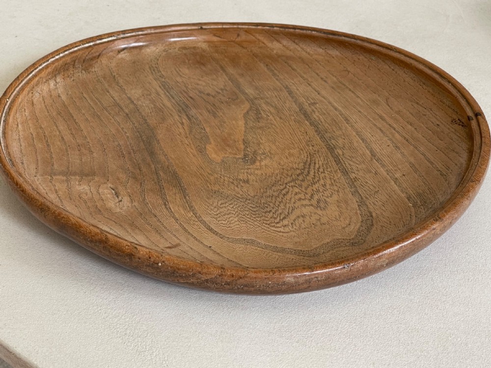 A large, shallow circular antique platter crafted from turned ash wood displaying prominent natural grain patterns. View VII