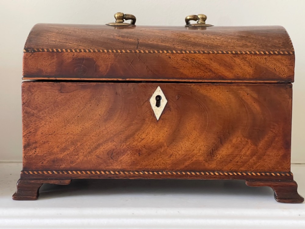A rectangular Georgian flame mahogany tea caddy with a domed lid, brass carrying handles, and a bone keyhole escutcheon.
