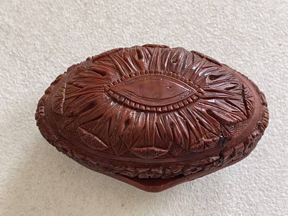 An oval-shaped dark brown coquilla nut snuff box featuring an intricate high-relief carved scene of a seated figure with a writing desk and stylized trees. View IV