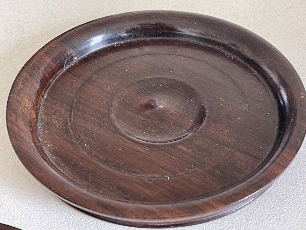 A pair of circular turned dark rosewood wine bottle coasters with raised rims and recessed centres. View II