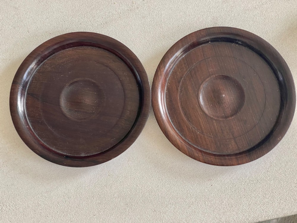 A pair of circular turned dark rosewood wine bottle coasters with raised rims and recessed centres. View V