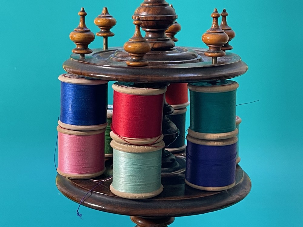 A turned dark wood antique sewing reel stand featuring multiple tiers for thread spools and a cushioned top. View III