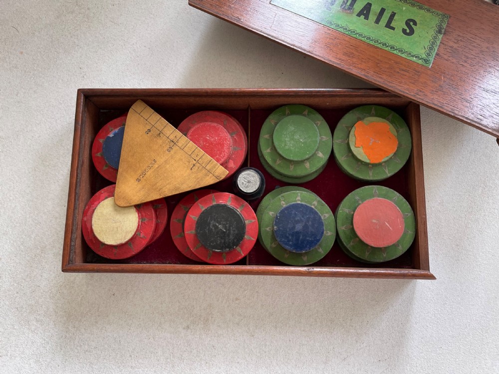 An open wooden mahogany box containing a Victorian squails game set with colourful turned wooden discs and a triangular wooden swoggle measuring tool.