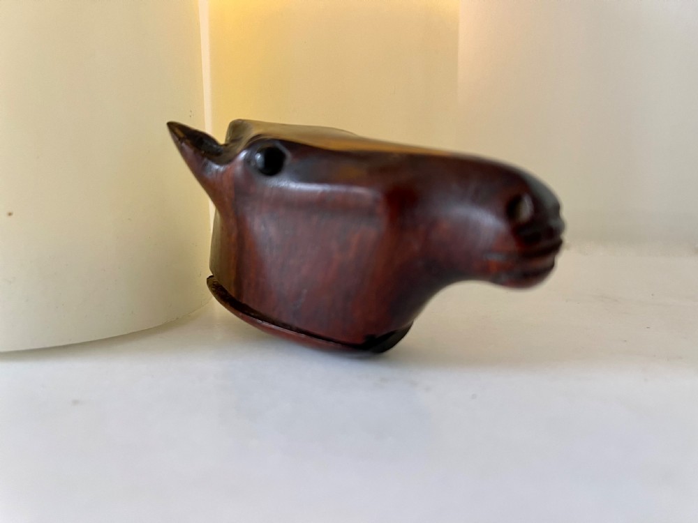 A hand-carved dark wood snuff box shaped in the detailed form of a horse head with a hinged opening at the base.