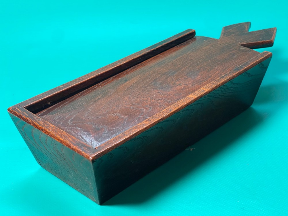 A dark carved oak tinder box with a sliding top lid and a shaped geometric end handle.