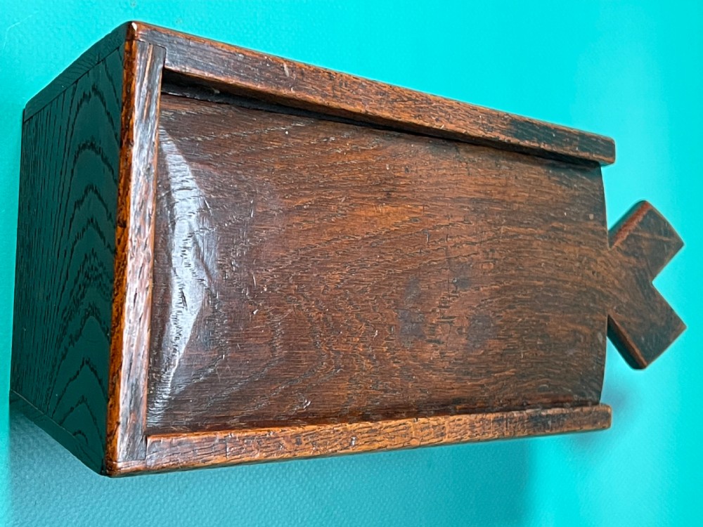 A dark carved oak tinder box with a sliding top lid and a shaped geometric end handle. View V