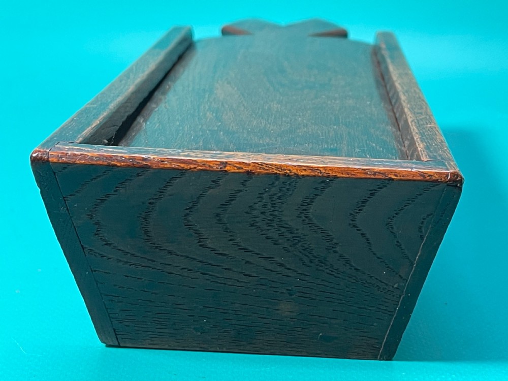 A dark carved oak tinder box with a sliding top lid and a shaped geometric end handle. View VI